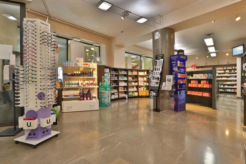 Interno della Farmacia Asquini Alla Fenice Risorta con pavimento in marmo, scaffali di prodotti ed espositore di occhiali Utilissimi